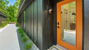 A modern building with a dark exterior, a glass door with an orange frame, and a visible interior with a sink and countertop. - 500 House - Unit C 1 Bedroom Townhouse (Mequon)