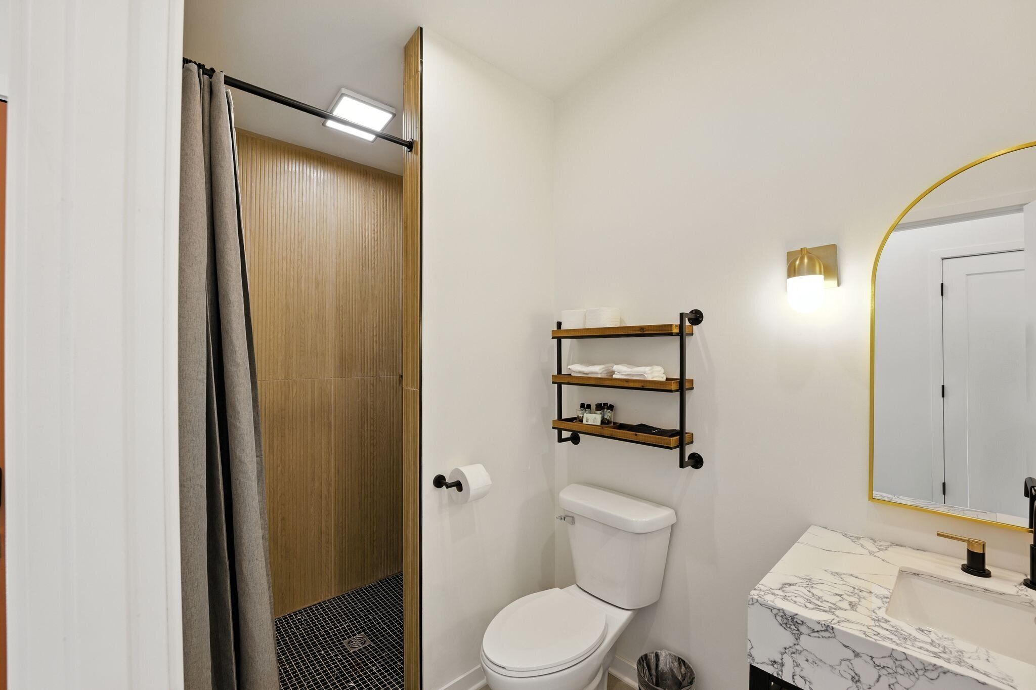 Une salle de bain comprenant des toilettes, un lavabo avec un plan de travail en marbre, une douche avec un rideau et une étagère contenant des articles de toilette.