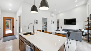 A modern kitchen with a central island, a dining area with a round table, and a living room with a gray sofa. - 500 House - Unit D 2 Bedroom Townhouse (Mequon)