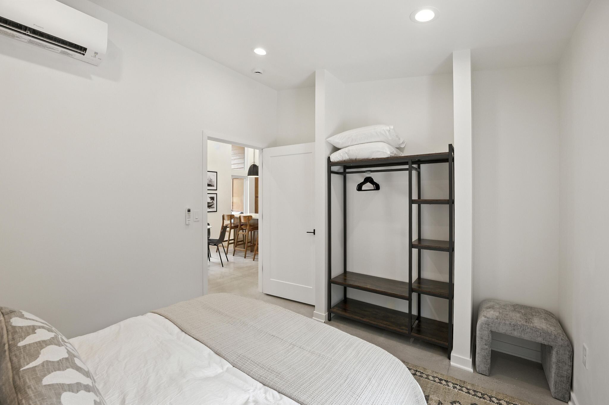 Un dormitorio con cama, armario, banco y puerta que da a un comedor.