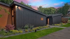 A modern building with a dark exterior, a wooden section on the left, and a well-maintained garden with various shrubs and a pathway leading to the entrance. - 500 House - Unit D 2 Bedroom Townhouse (Mequon)