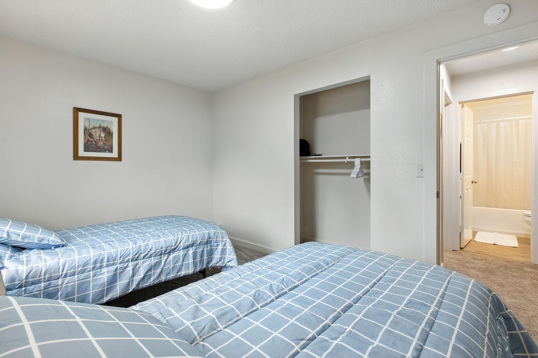 Ein Schlafzimmer mit zwei Betten, einem Kleiderschrank und einem durch eine offene Tür einsehbaren Badezimmer.