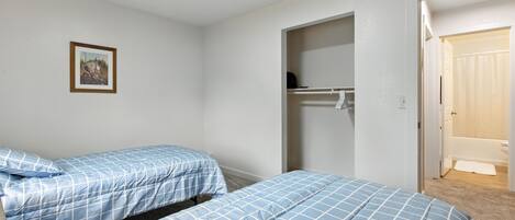 Ein Schlafzimmer mit zwei Betten, einem Kleiderschrank und einem durch eine offene Tür einsehbaren Badezimmer.