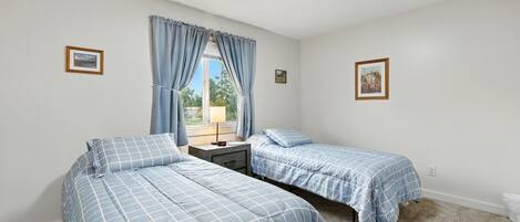 A bedroom with two beds, a window with curtains, a nightstand, and a picture on the wall.