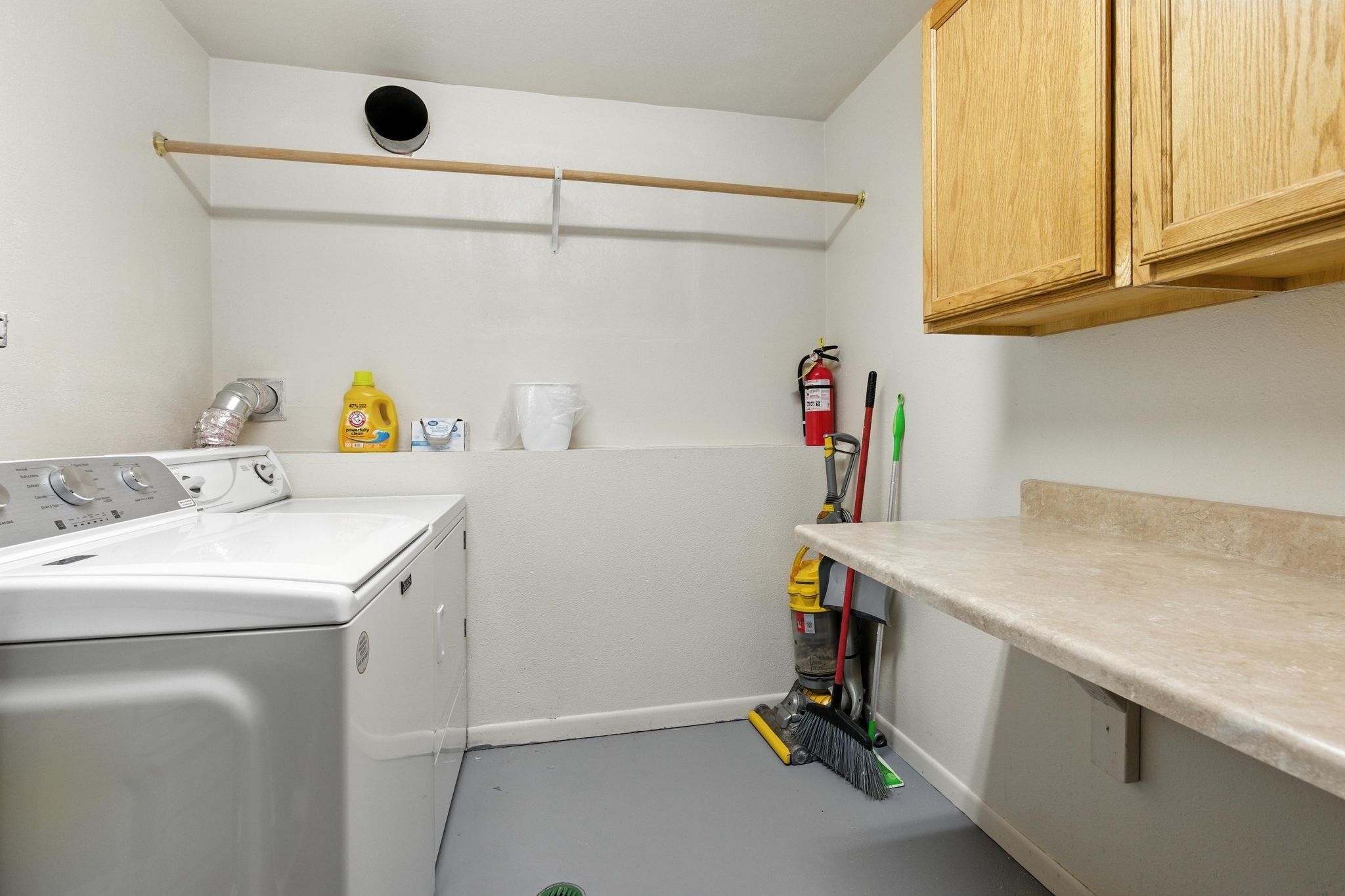 A laundry room with a washing machine, a fire extinguisher, cleaning supplies, and a broom.