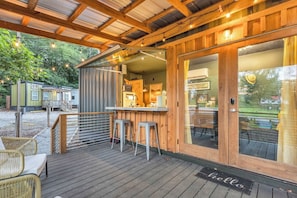A wooden deck with a bar area, outdoor seating, and a view of a green landscape.