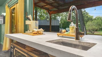A kitchen with a large countertop, a sink, and a hanging faucet. There are cabinets below the countertop and a window with curtains.