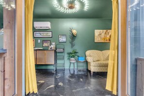 A room with a sofa, a plant, a wall-mounted air conditioner, and a ceiling light fixture. - The Sassafras - Shipping Container, shared Hot Tub (Easley)