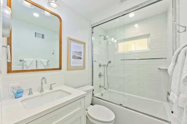 Un baño moderno con ducha de vidrio, un lavamanos blanco con espejo y un cuadro enmarcado en la pared.