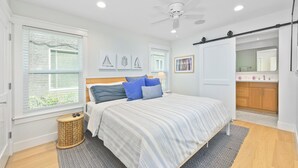 Un dormitorio moderno con cama, ventilador de techo y baño visible a través de una puerta abierta.