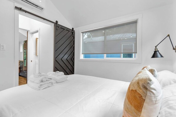 Un dormitorio con cama, ventana con persianas, lámpara y puerta corredera.