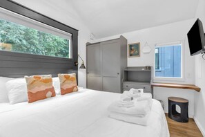 Een moderne slaapkamer met een groot bed, een grijze garderobe, een aan de muur bevestigde televisie en een raam met uitzicht op bomen.