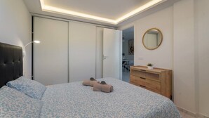 A bedroom with a bed, a wardrobe, a vanity with a mirror, and a door leading to another room.