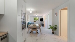 A modern kitchen with built-in appliances, a dining area with a marble floor, and a TV in the background.