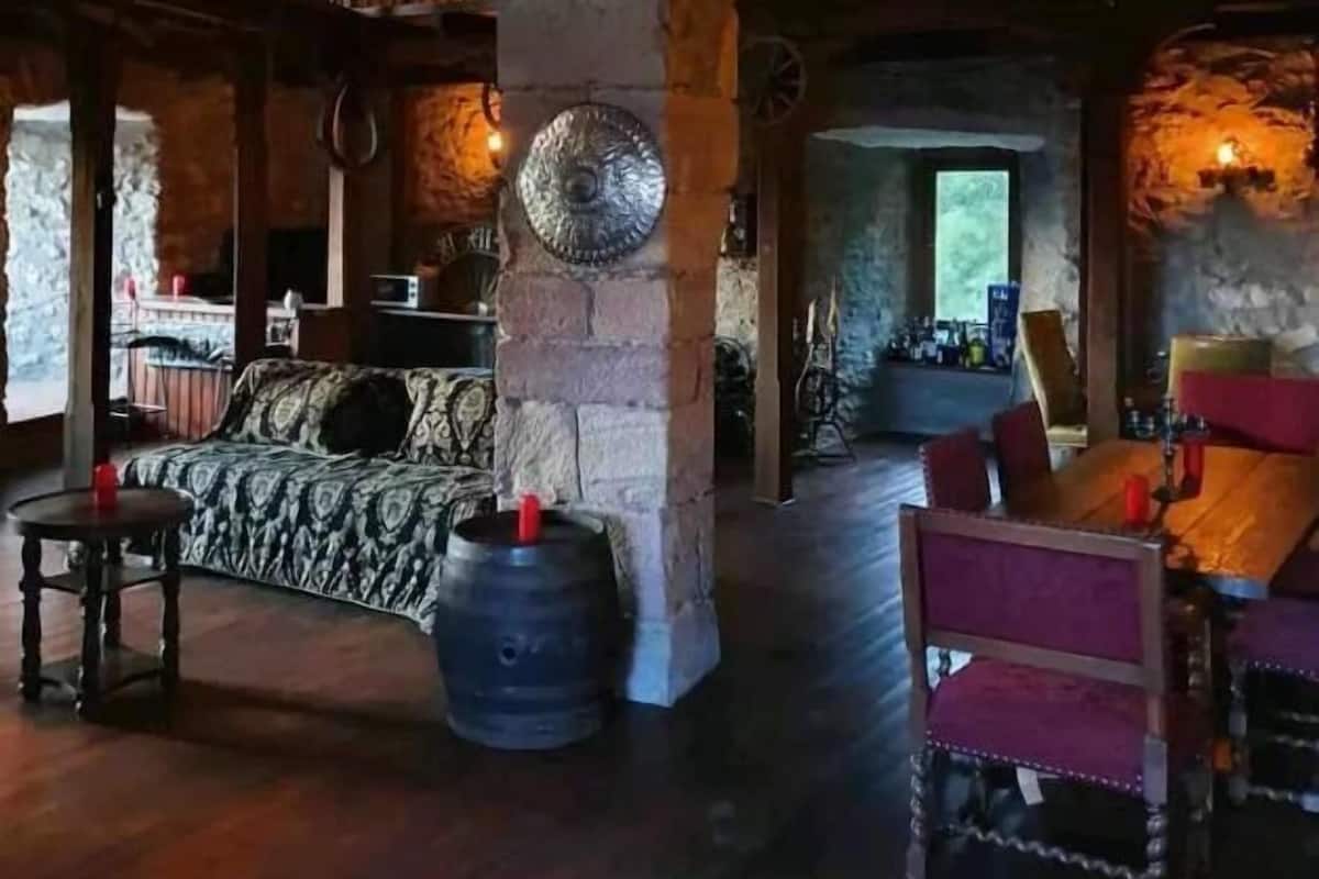 A rustic interior with stone pillars, wooden furniture, and a balcony.