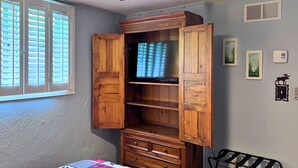 Ein Zimmer mit einem Holzkasten, einem Deckenventilator, einem Fenster mit Jalousien und einem an der Wand montierten Thermostat.