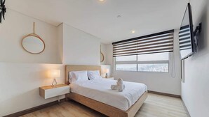 Ein modernes Schlafzimmer mit einem hölzernen Bett, Nachttischen, einem runden Spiegel und Blick auf die Stadt durch das Fenster.