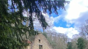 Un edificio de piedra con un pequeño ventanal arqueado y una valla metálica al frente.