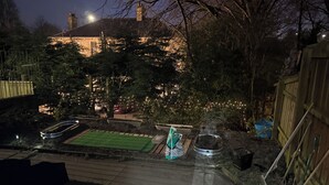 Un patio trasero con zona pavimentada, un pequeño jardín y una valla de madera.