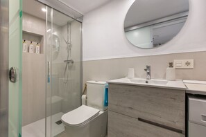 A modern bathroom with a glass-enclosed shower, a toilet, a sink with a mirror, and a wooden vanity.