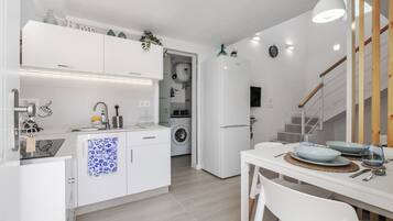 Una cocina moderna con muebles blancos, lavadora incorporada y un comedor con una mesa preparada para dos.