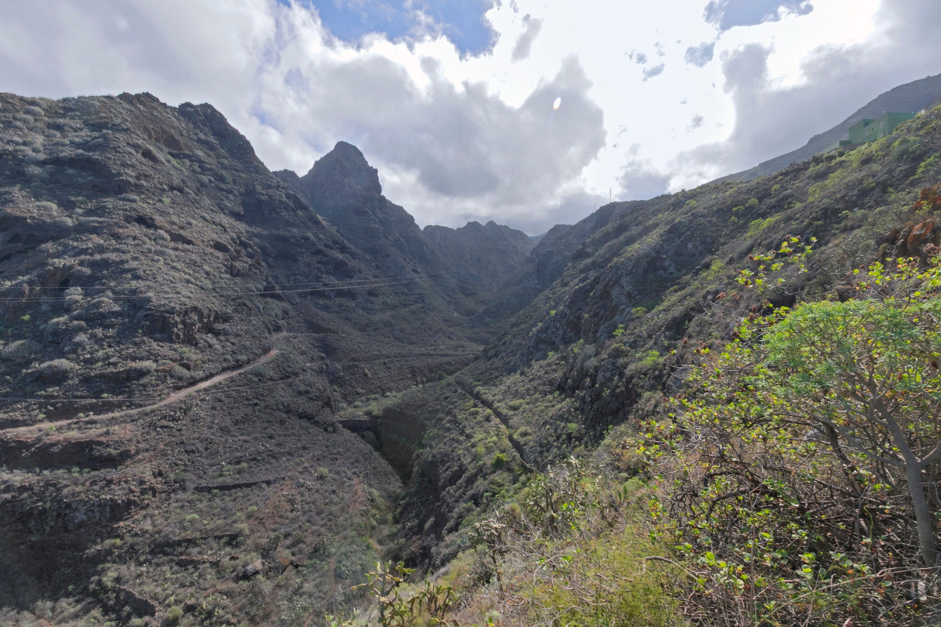 A mountainous landscape with a valley, a winding path, and sparse vegetation.