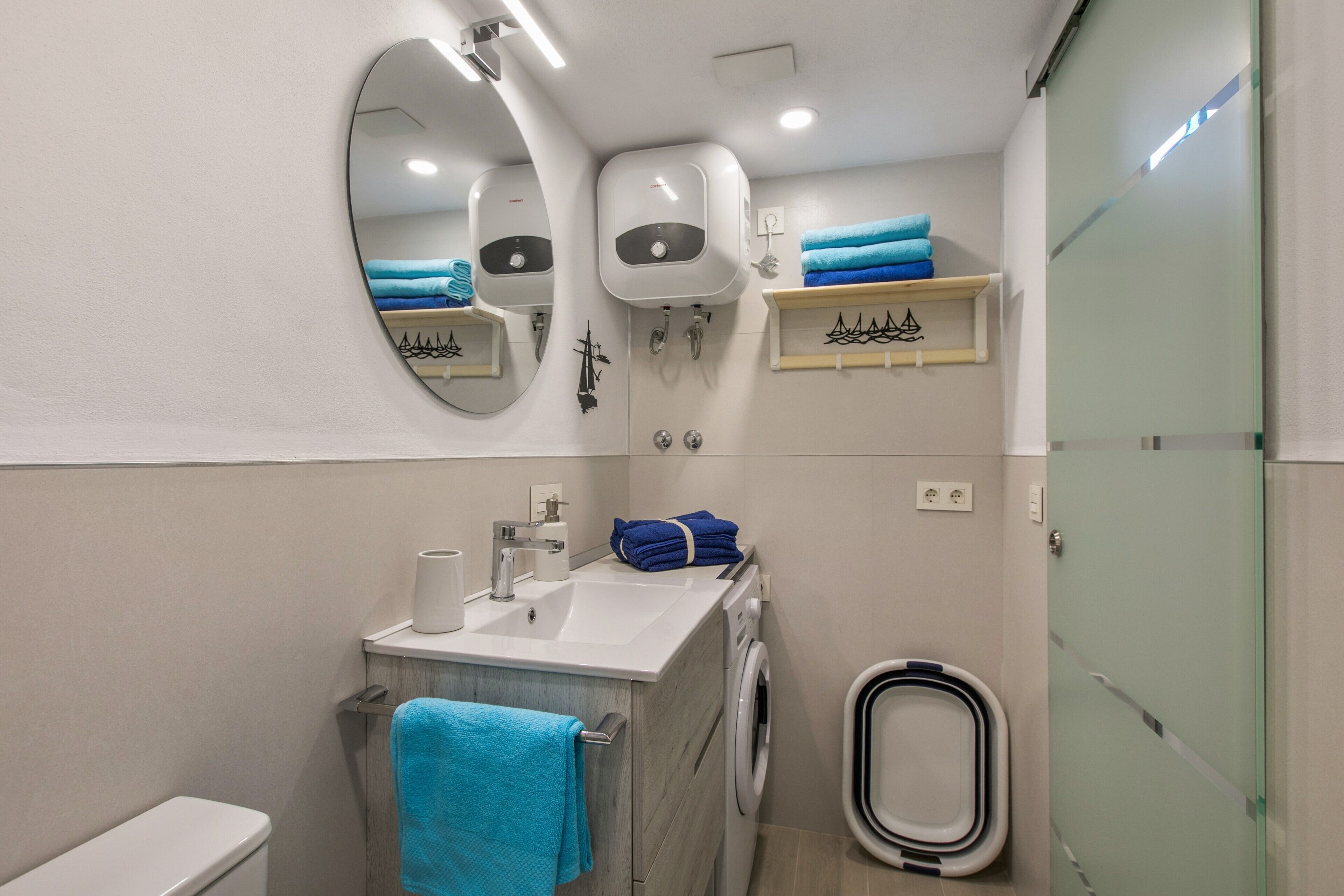 Une salle de bain moderne comprenant des toilettes, un lavabo, un miroir, un porte-serviettes et une douche à parois de verre.
