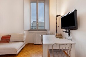A modern living room with a sofa, a dining table, chairs, a flat-screen TV mounted on the wall, and a window. - Quiet, Modern Apartment in CityLife, Close to the Center (Milano)