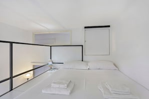 A single bed with white linens and towels, a bedside table with a lamp, and a window with a view. - Quiet, Modern Apartment in CityLife, Close to the Center (Milano)