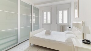 A bedroom with a bed, a bedside table, a lamp, a wardrobe, and a window.
