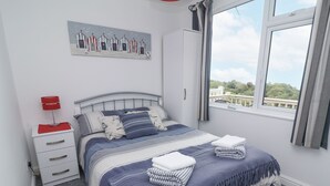 A bedroom with a bed, a nightstand, a window with a view, and a painting on the wall. - I C Lundy Too (Bideford)