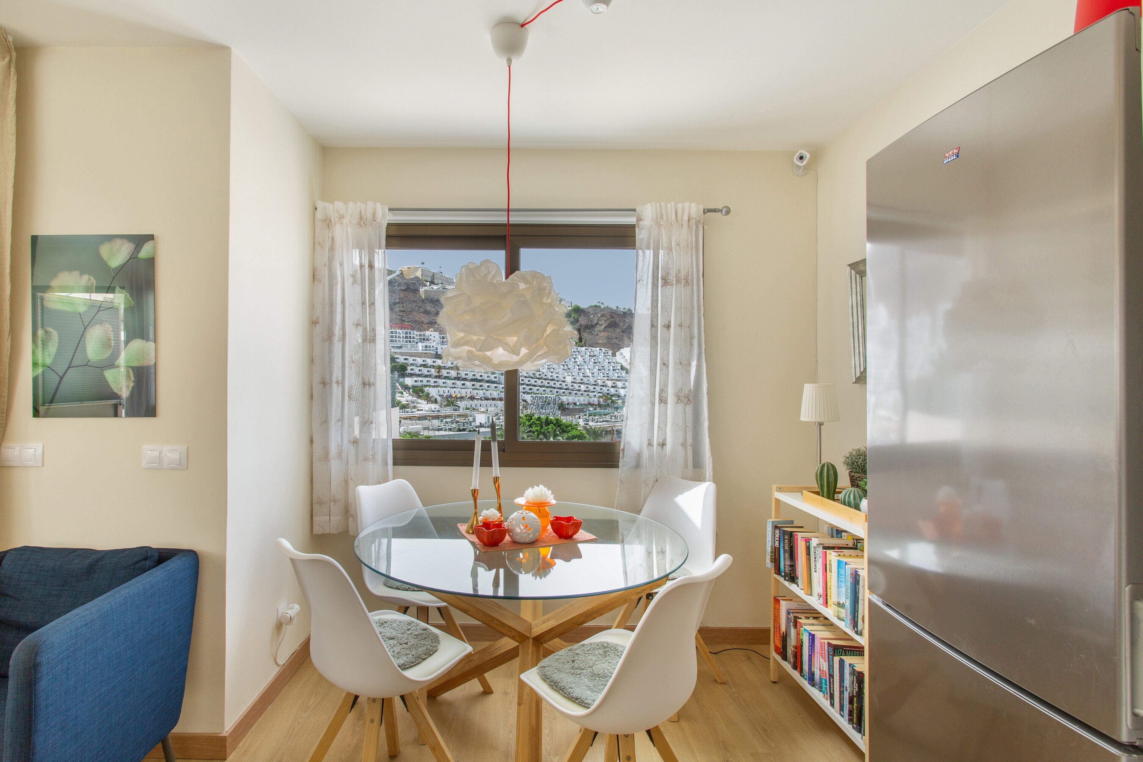 Una cocina compacta con una mesa de comedor, sillas, un refrigerador y una estantería.