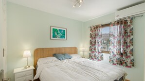 Ein Schlafzimmer mit einem Bett, Nachttischlampen, einem Nachttisch, einem gerahmten Bild an der Wand und einem Fenster mit blumigen Vorhängen.