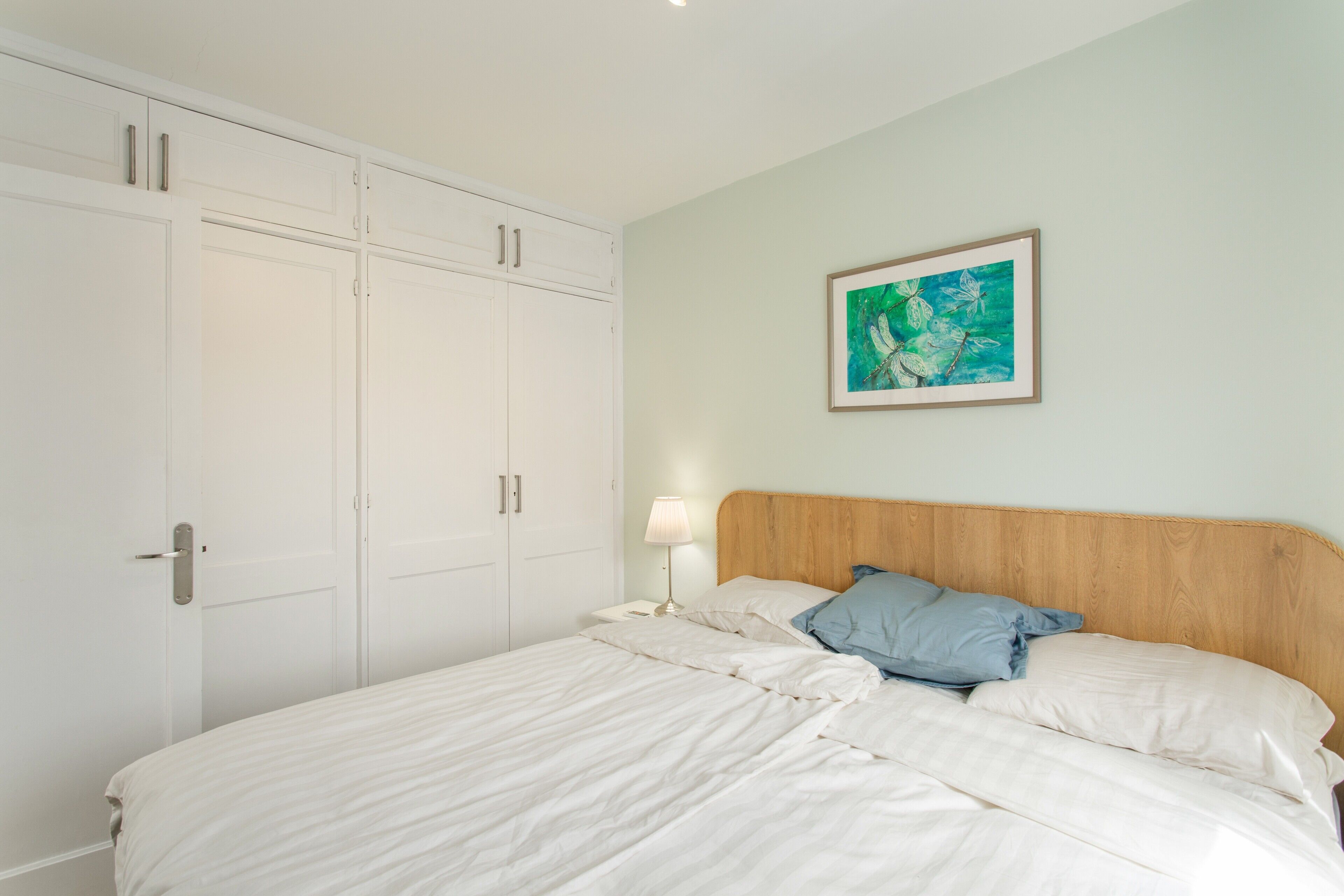 Ein Schlafzimmer mit Bett, Nachttisch, Lampe, einem gerahmten Bild an der Wand und einem Kleiderschrank.