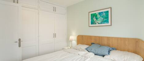 Ein Schlafzimmer mit Bett, Nachttisch, Lampe, einem gerahmten Bild an der Wand und einem Kleiderschrank.