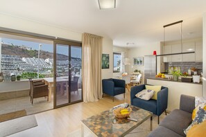 Una sala de estar moderna con una mesa de centro de vidrio, sofás azules y vistas a un paisaje urbano a través de amplios ventanales.