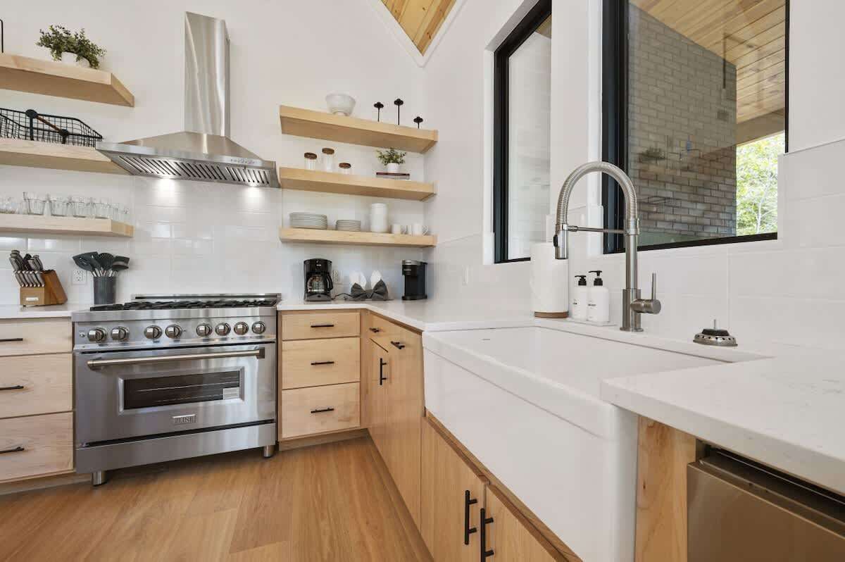 A modern kitchen with white cabinetry, stainless steel appliances, and wooden shelves.