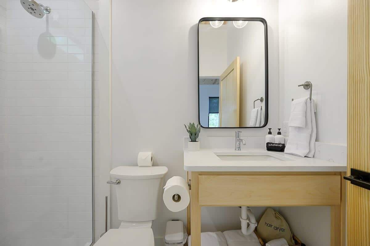 A modern bathroom with a toilet, sink, mirror, and shower.