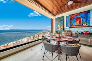 Un comedor con vistas al mar y al paisaje urbano, con una mesa redonda, sillas y una parrilla.