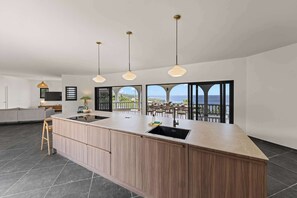 A modern kitchen with a central island, pendant lighting, and large windows offering ocean views. - Villa Barbulete | Clifftop Infinity Pool & Views (Cas Abou)