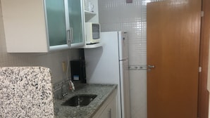 Une cuisine avec des meubles blancs, un plan de travail en granit, un four à micro-ondes, un réfrigérateur et une porte en bois.