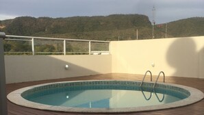 Une piscine sur une terrasse en bois, avec vue sur une colline boisée.