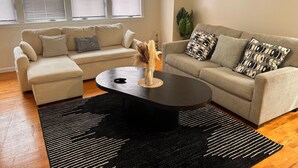 Een woonkamer met twee beige banken, een zwarte salontafel en een zwart-wit gestreept vloerkleed.