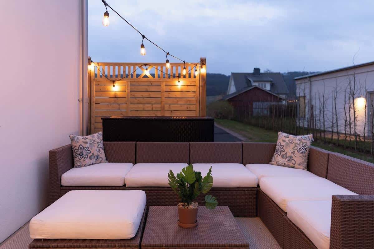 A cozy outdoor seating area with a wicker sofa, cushions, and a small table with a potted plant.