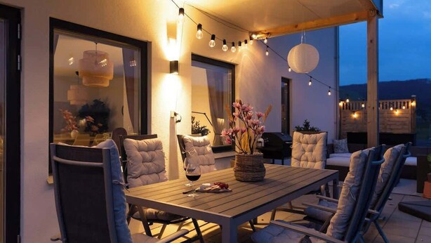 An outdoor dining area with a wooden table and chairs, string lights, and a view of the mountains. - Fully Equipped Home in Bastad with Cozy Patio (Båstad)
