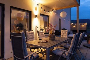 An outdoor dining area with a wooden table and chairs, string lights, and a view of the mountains.