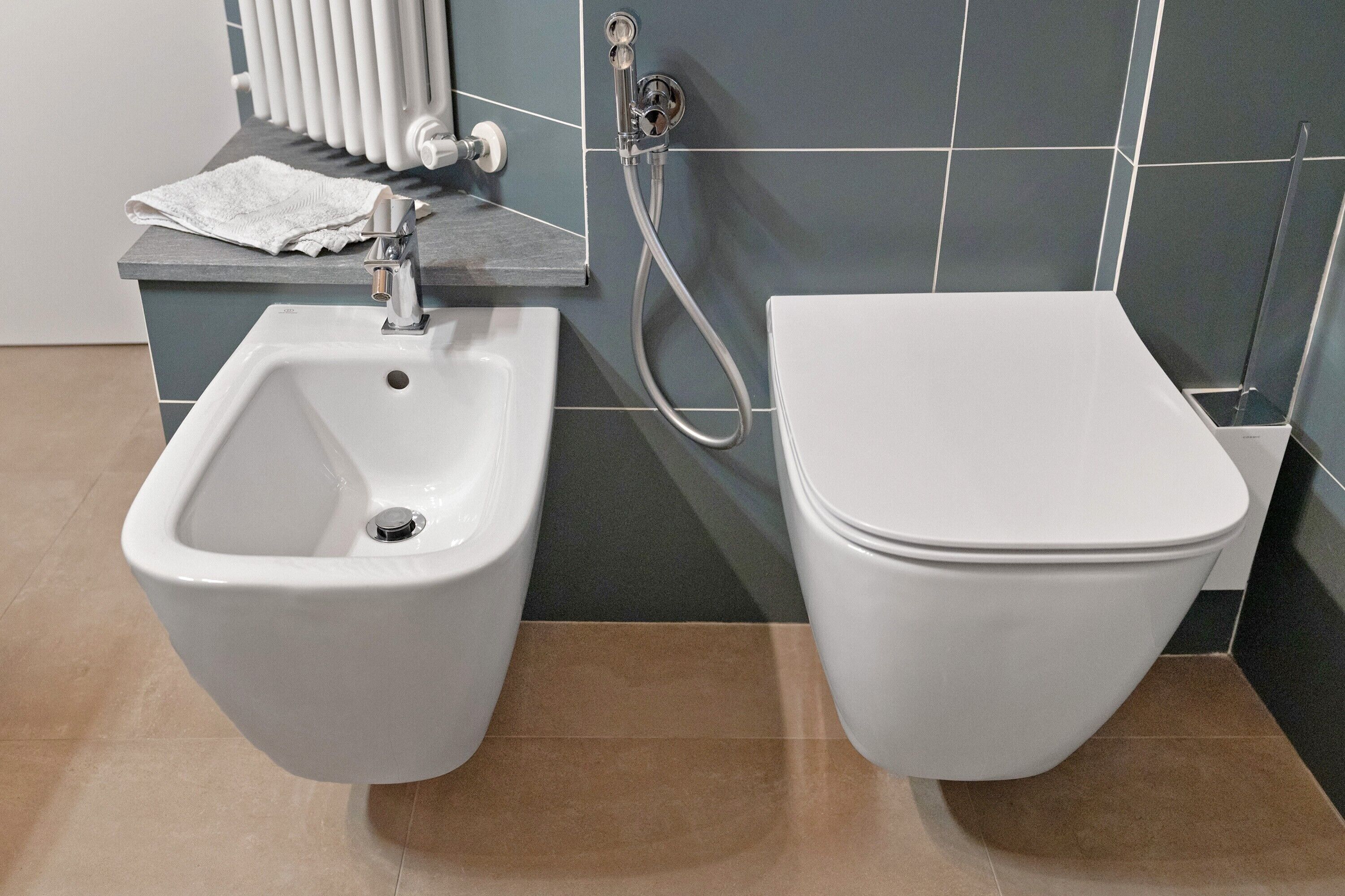 A bathroom with a bidet, a toilet, a towel, and a radiator.