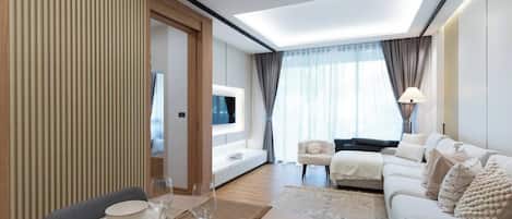 A modern hotel room with a dining area, a sofa, a TV, and a large window with curtains.