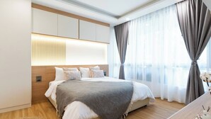 Een moderne slaapkamer met een groot bed, een houten hoofdbord en uitzicht op de stad door dunne gordijnen.