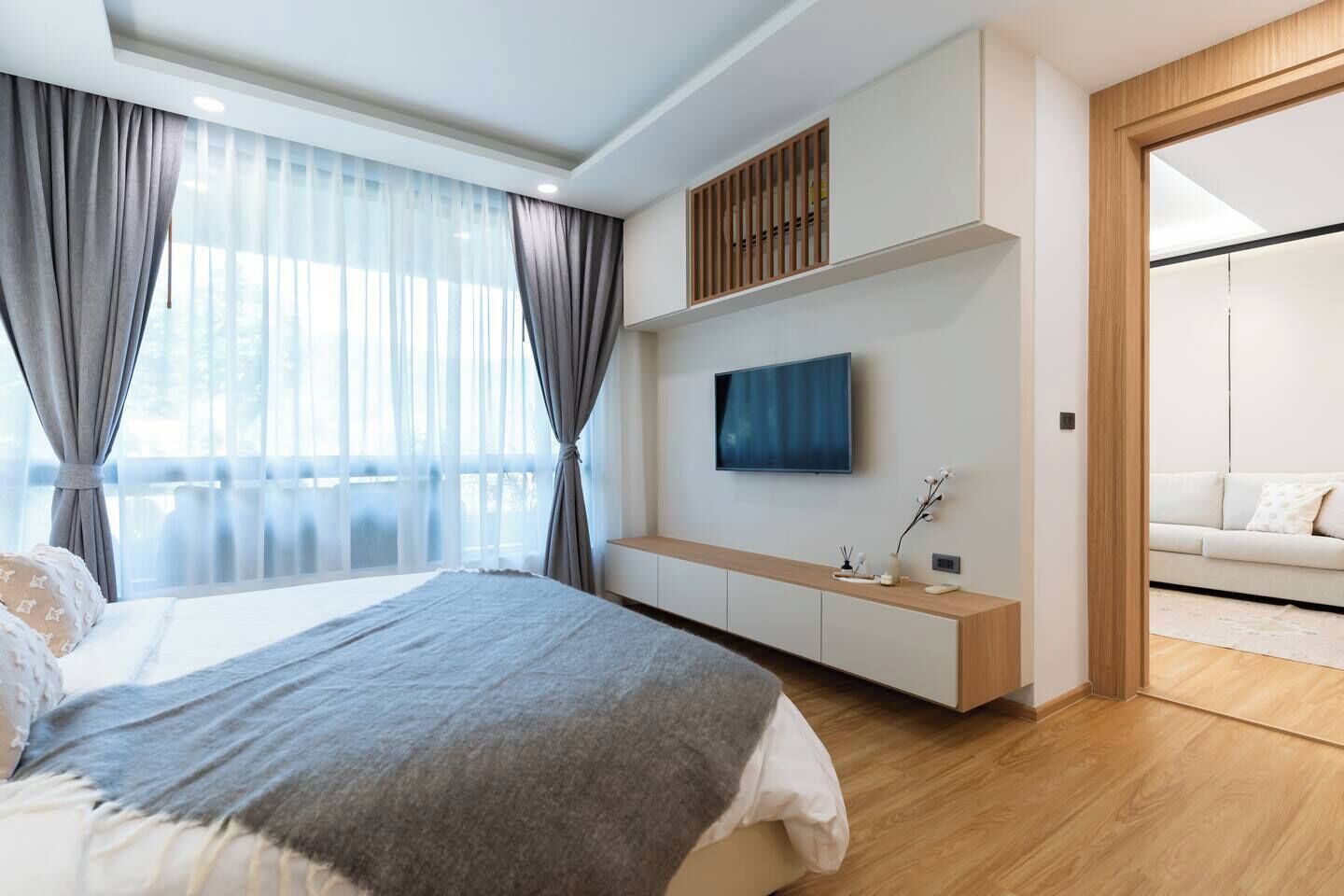 Un dormitorio moderno con cama, televisor, banco empotrado y vistas a un balcón.